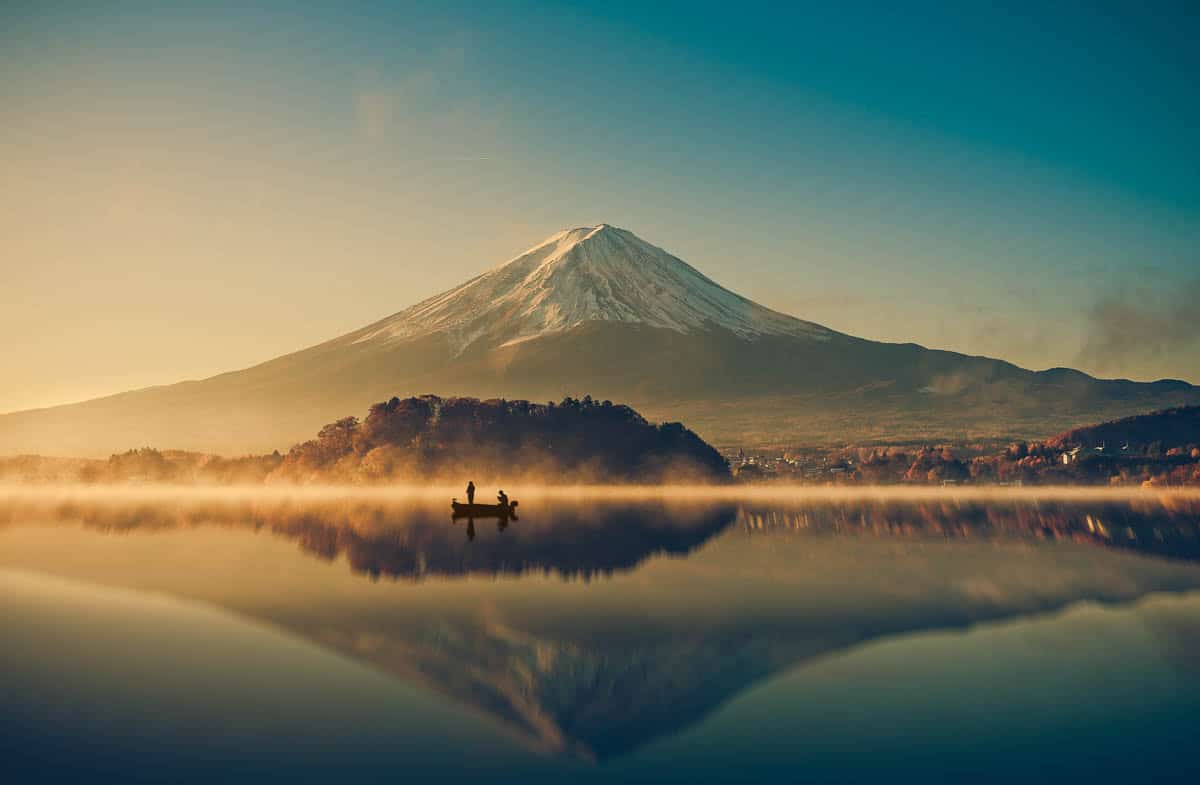 A small fishing boat crosses misty water beneath Mount Fuji in Japan.